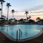 A serene poolside scene at sunset with palm trees.