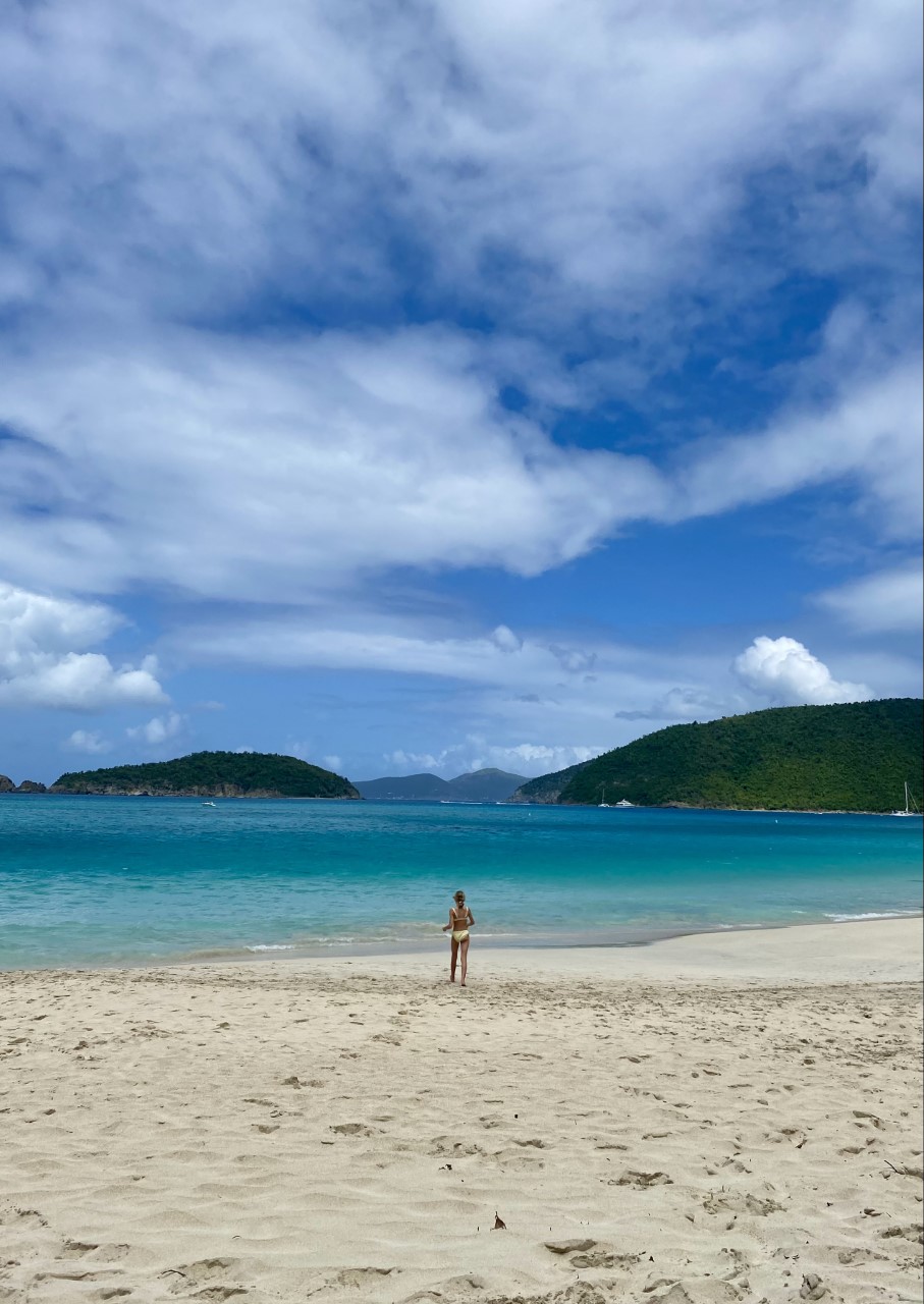 A person standing on a sandy beach under a blue sky with scattered clouds.